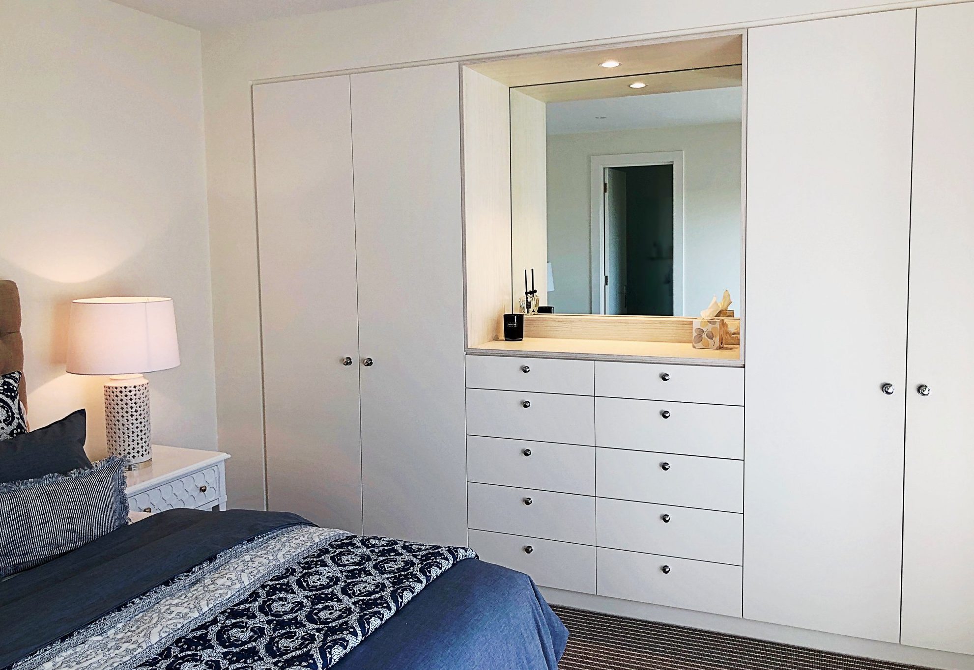 White built-in wardrobes around a dressing nook with drawers and a lit mirror
