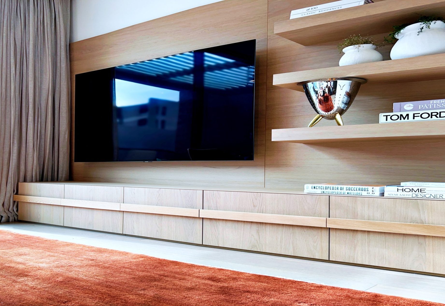 Wall-mounted TV on a timber panel wall with floating shelves and a long low cabinet