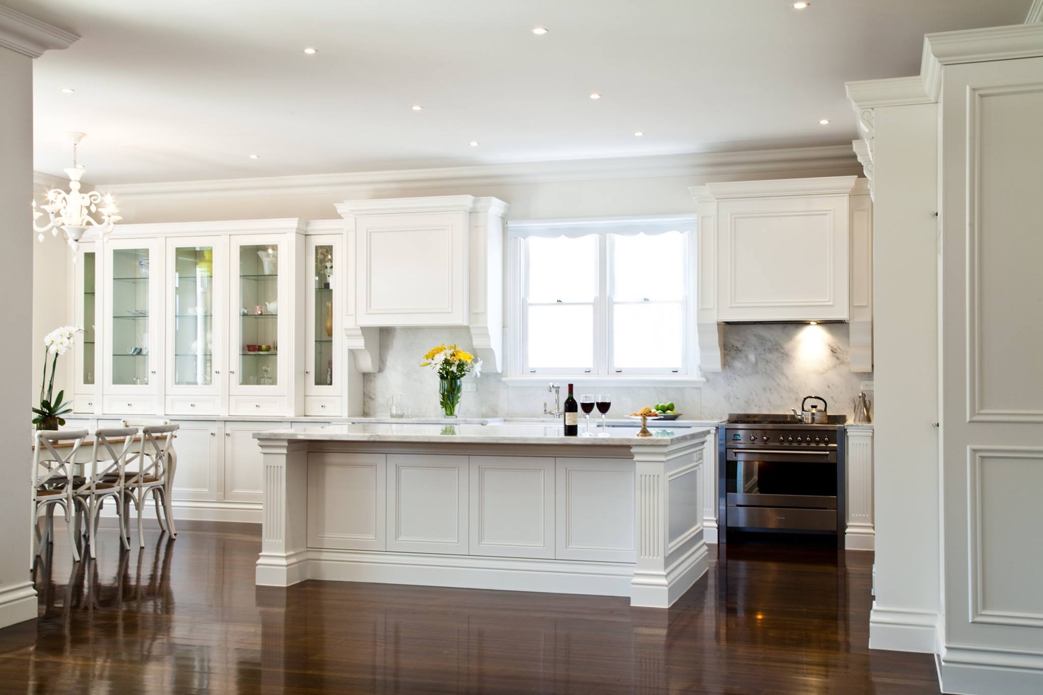 White classic-style kitchen with marble-topped island, glass display cabinets and dark floors
