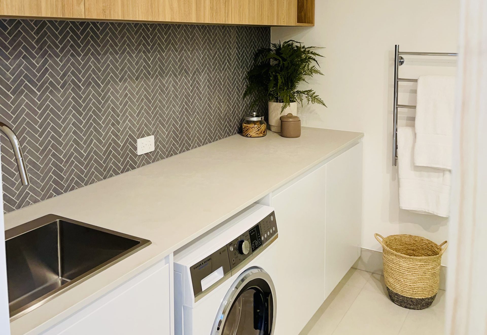 Wide view of a laundry with stone benchtop, herringbone splashback and front-loading washer