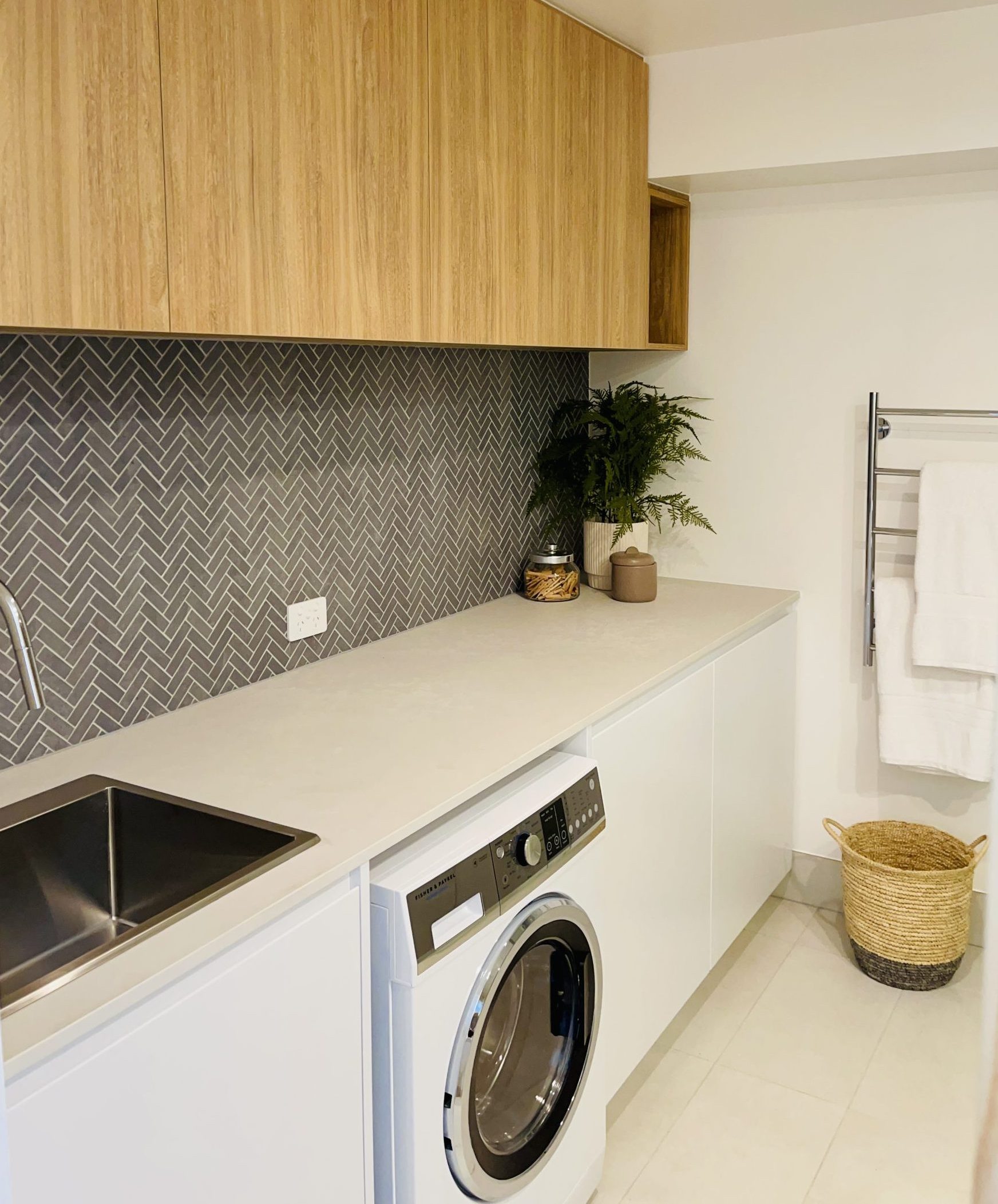Laundry with timber overhead cupboards, herringbone tiles, sink and front-loading washer
