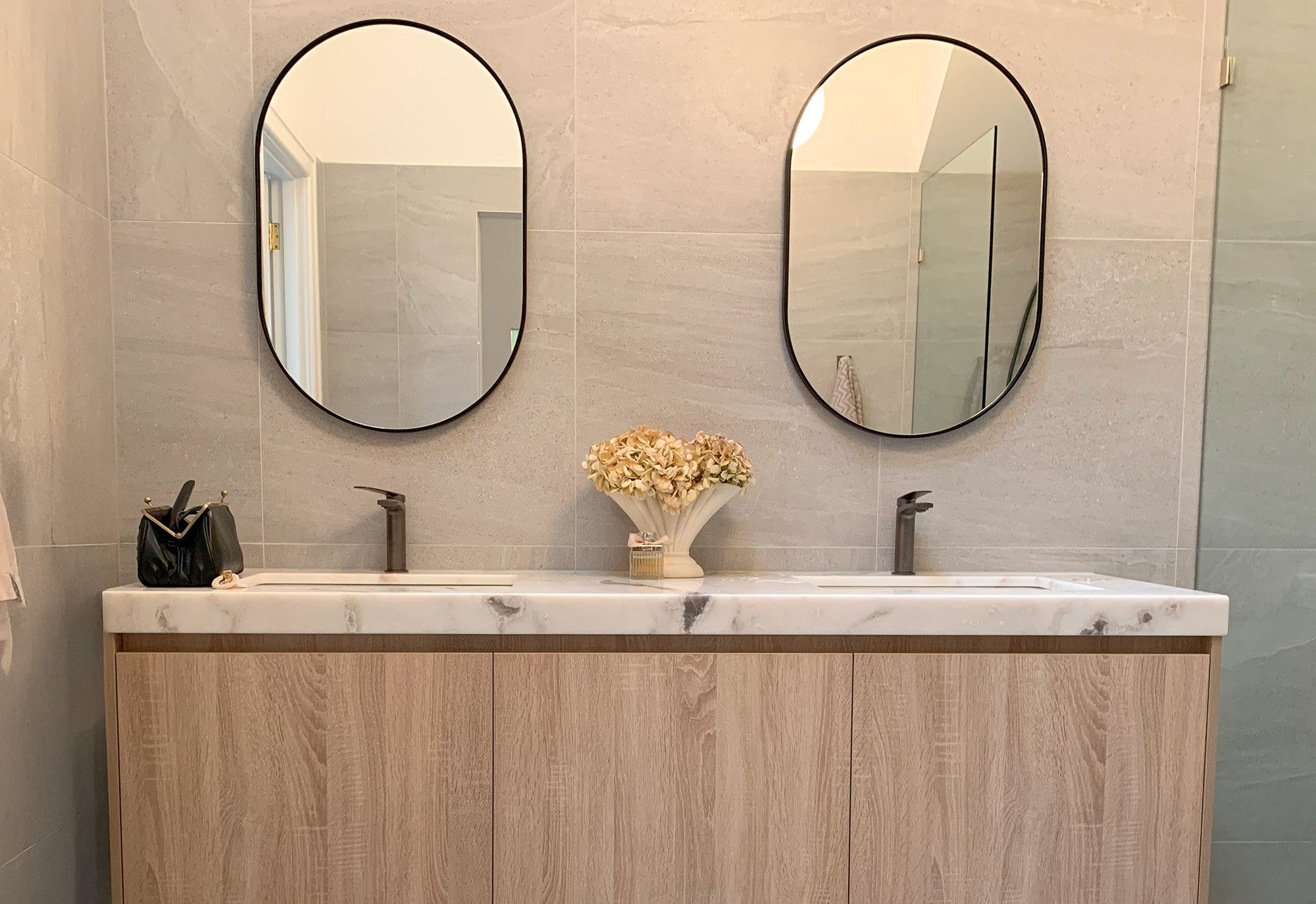 Closer view of a timber-look double vanity with marble top, basins and oval mirrors