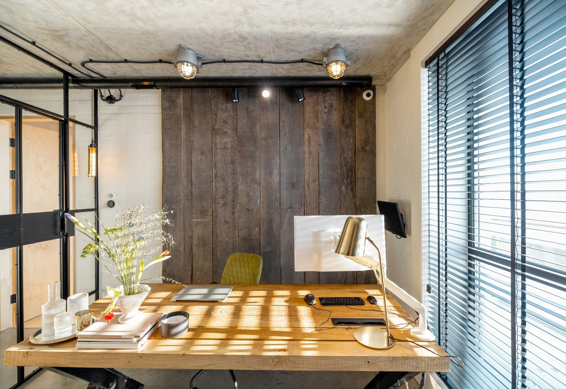 Rustic timber desk in a home office with a dark timber wall and window blinds