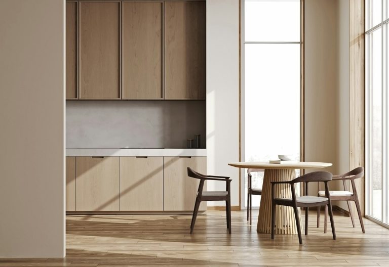 Light timber kitchen cabinets and round dining table beside tall windows